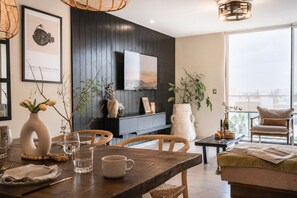 A dining area with a wooden table, chairs, a vase with flowers, a television, and a view of the outdoors. - Wabi Sabi 3 BedRoom / Daily Clean (Guadalajara)