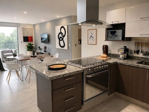 Cozinha moderna com bancada de granito, eletrodomésticos de aço inoxidável e uma área de jantar com mesa e cadeiras.