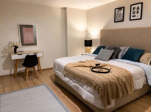 Ett sovrum med en säng, ett sängbord, en lampa, ett skrivbord, en stol och konstverk.