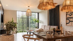 A modern dining area with a wooden table set for two, surrounded by wicker chairs, a large potted plant, and a sofa. - Urban minimalist 3 BedRoom / Daily Cleaning (Guadalajara)