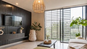 A modern living room with a large TV, a large window with blinds, a sofa, a coffee table, and a hanging light fixture. - Urban minimalist 3 BedRoom / Daily Cleaning (Guadalajara)