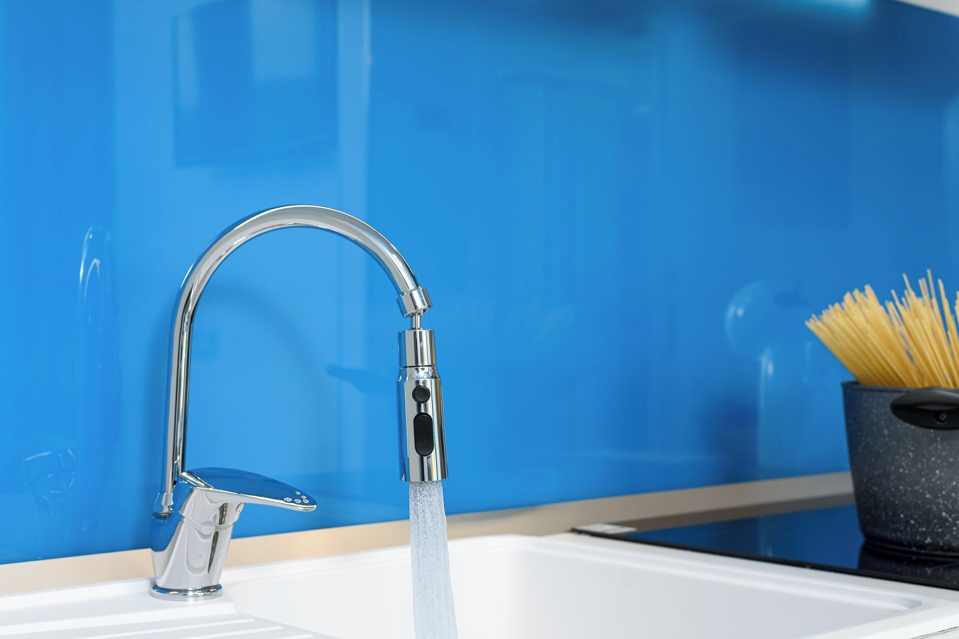 A modern kitchen with a chrome faucet, a white sink, and a blue backsplash.