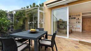 A patio with a table and chairs, a glass door leading to a room with a bookshelf, and a stone wall.