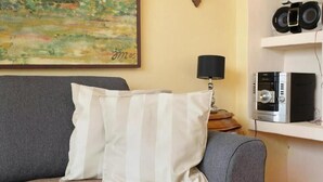A living room with a grey sofa, a striped pillow, a painting on the wall, a lamp, and a shelf with audio equipment.