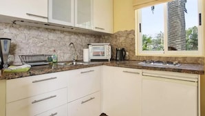 A compact kitchen with white cabinets, a stone backsplash, a window with a view of palm trees, a built-in toaster, and a coffee maker.