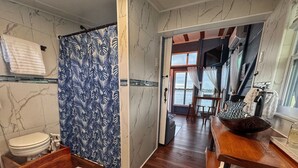 A bathroom with a toilet, a shower with a blue leaf pattern, wooden flooring, and a view of the outdoors through a window. - The Burrow, an amazing floating cabin with pontoon rental available (Grant-Valkaria)
