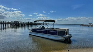 A pontoon boat docked at a pier with a clear sky and calm water. - The Burrow, an amazing floating cabin with pontoon rental available (Grant-Valkaria)