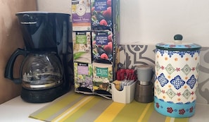 A kitchen area with a Hamilton Beach coffee maker, a box of herbal tea, a spice container, and a decorative ceramic pot. - 1 Block to Beach, Garden, Air, Kitchenette, C4 (Holbox)