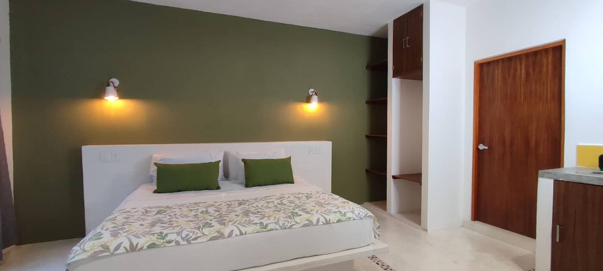 A bedroom with a bed, two wall-mounted lights, a wardrobe, and a door.