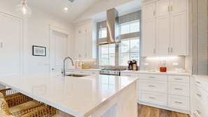 A modern kitchen with white cabinetry, a large island, stainless steel appliances, and a large window providing natural light. - Gorgeous family beach home with balcony and wonderful amenities (Port Aransas)