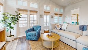 A spacious living room with a blue armchair, a beige sofa, and a round coffee table. - Gorgeous family beach home with balcony and wonderful amenities (Port Aransas)