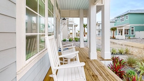 A covered porch with white wooden chairs and a view of neighboring houses. - Gorgeous family beach home with balcony and wonderful amenities (Port Aransas)