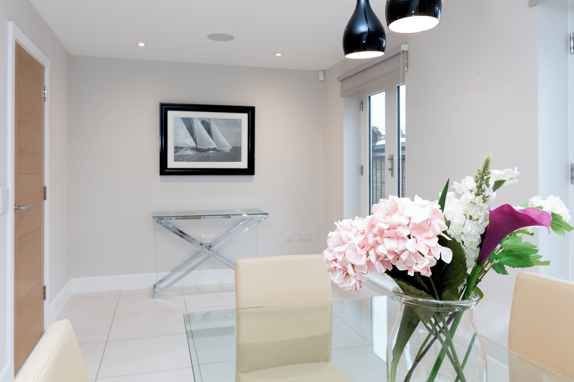 Un hall d’hôtel moderne avec une table en verre, une photographie encadrée accrochée au mur et un vase rempli de fleurs.