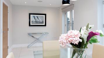 Un hall d’hôtel moderne avec une table en verre, une photographie encadrée accrochée au mur et un vase rempli de fleurs.
