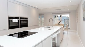 A modern kitchen with built-in appliances, a large island with a sink, and a view of the outdoors. - Stunning Central Windsor Town House (Windsor)