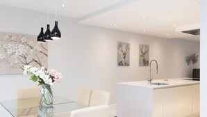 A modern kitchen with a central island, a glass dining table, and white cabinetry. - Stunning Central Windsor Town House (Windsor)