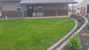 A building with a dark facade, a sloped roof, and a small porch area with two white chairs. - The Bunkhouse, charming 2-bedroom farmhouse (Priest River)