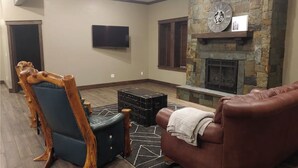 A living room with a stone fireplace, a flat-screen TV, and a leather couch. - The Bunkhouse, charming 2-bedroom farmhouse (Priest River)