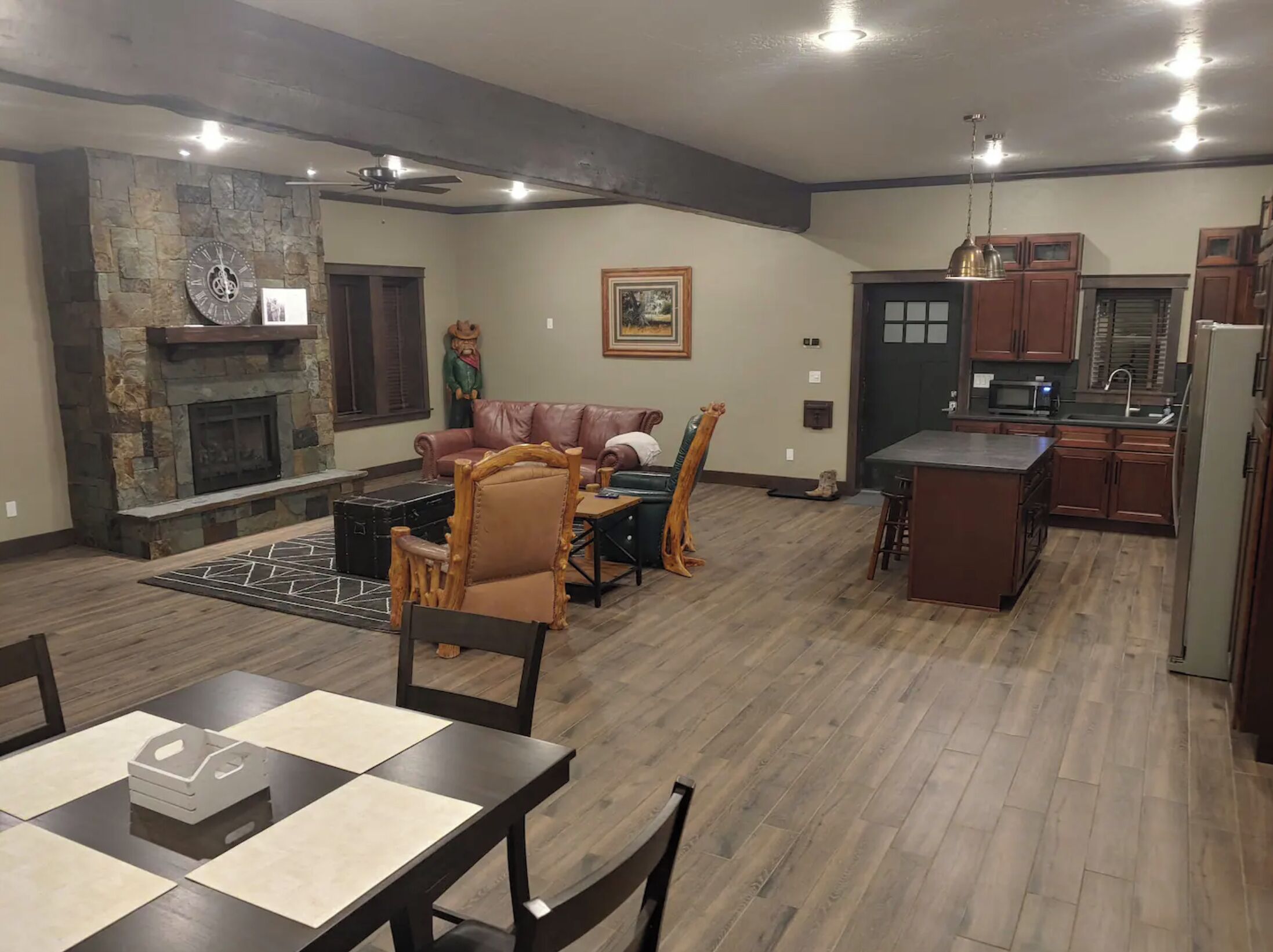 Amplia sala de estar con chimenea, comedor con mesa y sillas, cocina con armarios de madera y una pared de acento de piedra.