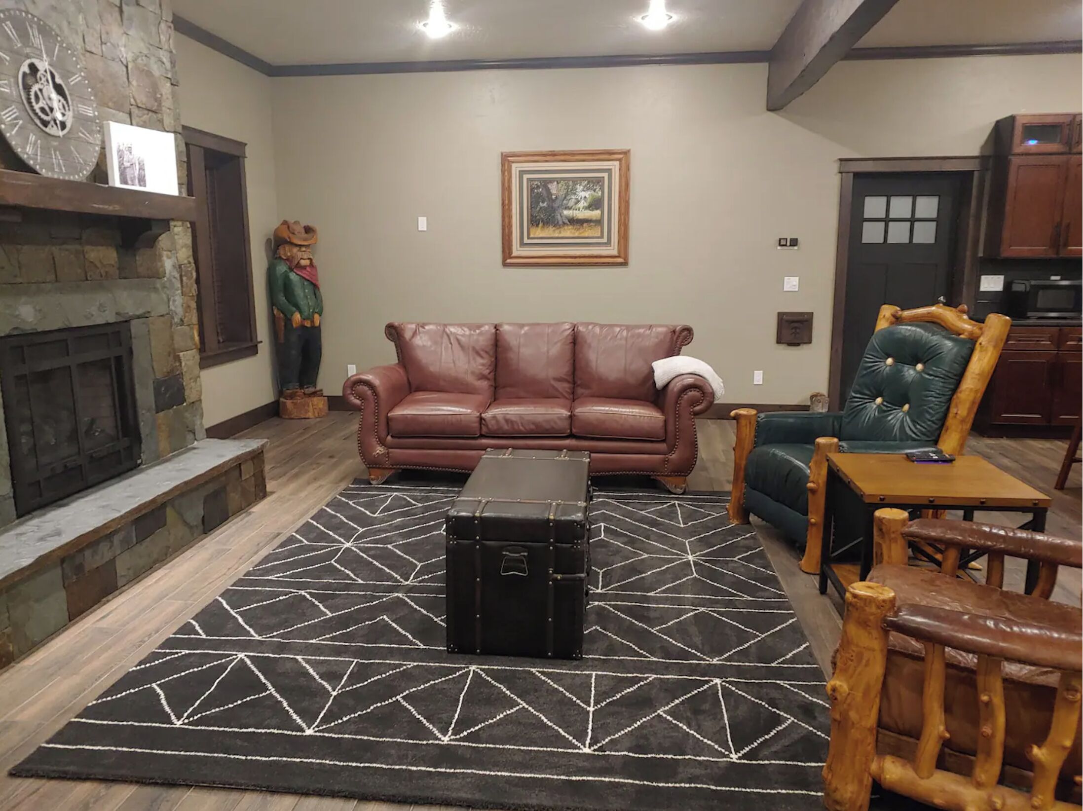 A living room with a stone fireplace, a brown leather sofa, a green armchair, and a black ottoman.