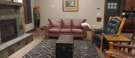 A living room with a stone fireplace, a brown leather sofa, a green armchair, and a black ottoman.
