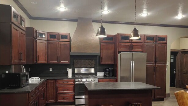A modern kitchen with dark wooden cabinets, stainless steel appliances, and a central island with stools. - The Bunkhouse, charming 2-bedroom farmhouse (Priest River)