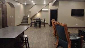 A spacious kitchen with a long counter and stools, a dining area with a table and chairs, a staircase leading to another level, and a TV mounted on the wall. - The Bunkhouse, charming 2-bedroom farmhouse (Priest River)