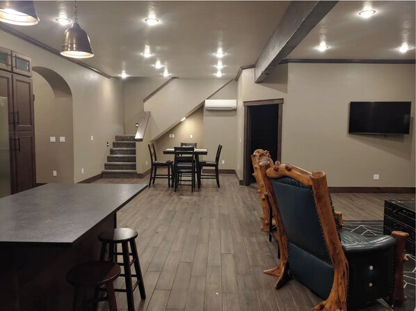 A spacious kitchen with a long counter and stools, a dining area with a table and chairs, a staircase leading to another level, and a TV mounted on the wall.