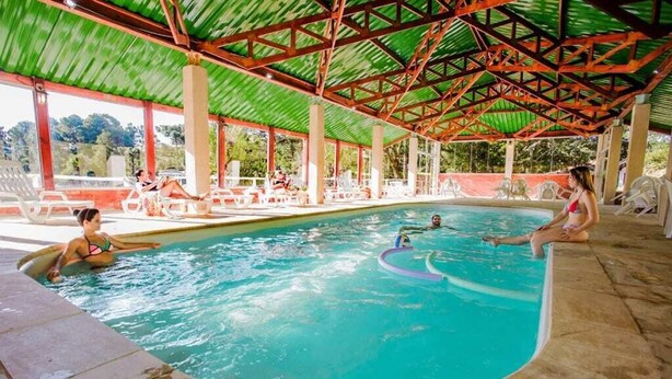 An indoor swimming pool with a covered area, lounge chairs, and a view of the outdoors. - Hotel Fazenda Floresta Negra (Camanducaia)