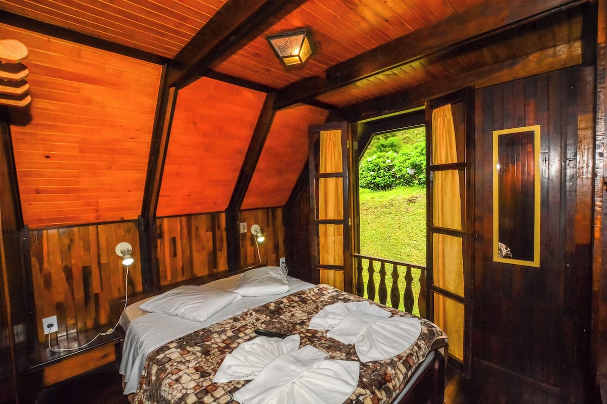 Una habitación de madera con una cama, un ventanal y vistas al verdor exterior.