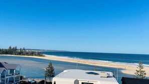A beachfront property with a view of the ocean, a sandy beach, and a residential area with houses and trees. - Ocean Views, Sundrift, Unit 18 (The Entrance)