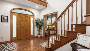 A wooden staircase with a welcome sign, a potted plant, and a door with a frosted glass panel.