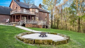 A large brick house with a balcony, a fire pit in the yard, and a stack of firewood.