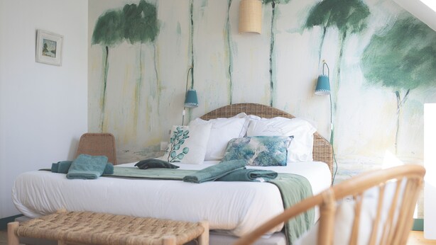 A bedroom with a bed, a chair, and a wall with a tree painting. - ESCALE DE GERBOLD (Gratot)