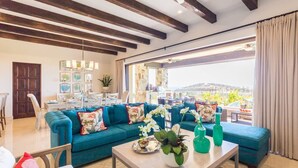 Ein modernes Wohnzimmer mit einem blauen Sofa, einem Couchtisch mit Dekoration und Blick ins Freie durch große Fenster.
