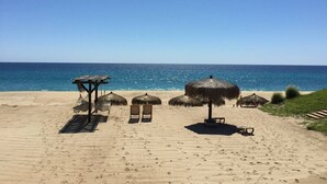 Ein Strand mit Reetsonnenschirmen und Holzstühlen.