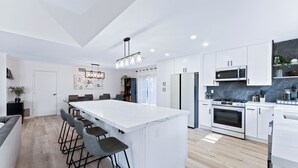 A modern kitchen with white cabinetry, a central island with bar stools, a built-in oven, and a microwave.
