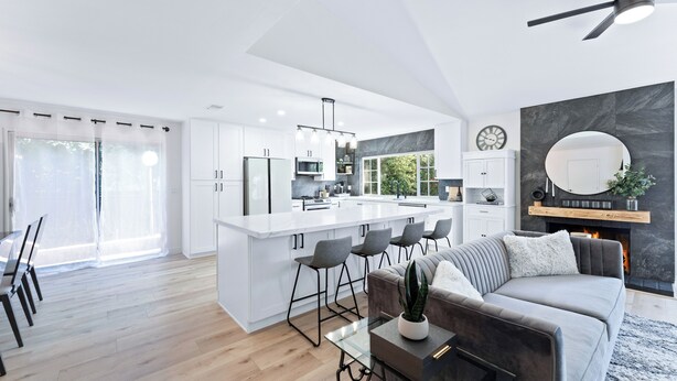 A modern kitchen with white cabinetry, a central island with bar stools, and a dining area with a glass table and chairs.