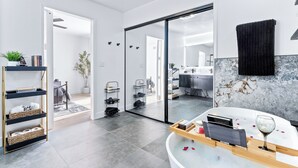 A modern bathroom with a marble countertop, a glass shower enclosure, and a black towel on the wall.