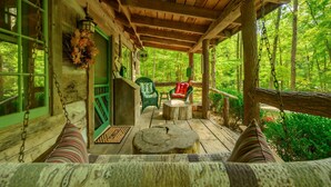 A wooden porch with a swing, green chairs, and a bench.