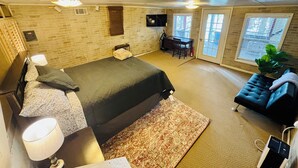 A bedroom with a bed, bedside table, lamp, and a desk with a chair.