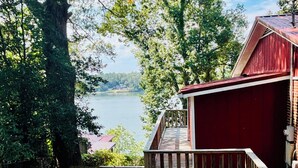 A wooden deck leading to a red building with a view of a lake and trees.