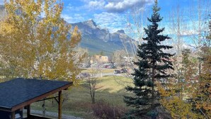 A covered outdoor seating area with a view of mountains and a small building in the distance. - Three Peaks Getaway 2 bedrooms & 2 bath-sleeps 6 (Canmore)