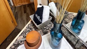 A bathroom with a wooden door, a towel rack with a towel, a basket with a towel, and a mirror with a blue vase and pampas grass. - Three Peaks Getaway 2 bedrooms & 2 bath-sleeps 6 (Canmore)