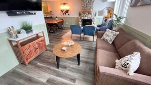 A modern living room with a flat-screen TV, a stone fireplace, a dining area with chairs, and a sofa with patterned cushions. - Three Peaks Getaway 2 bedrooms & 2 bath-sleeps 6 (Canmore)