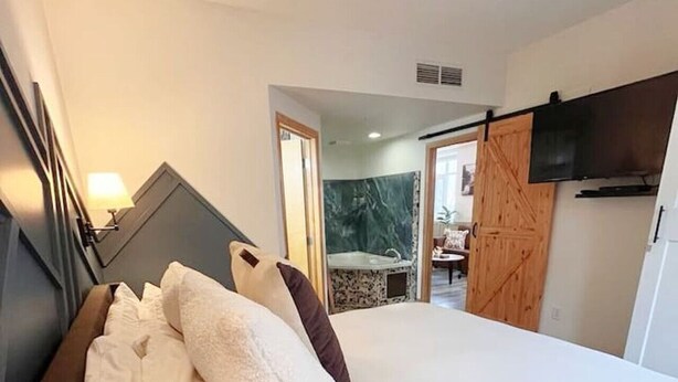 A bedroom with a large bed, a wooden door, and a television mounted on the wall. - Three Peaks Getaway 2 bedrooms & 2 bath-sleeps 6 (Canmore)