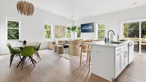 Een ruime keuken met een centraal eiland, grote ramen en een eethoek met groene stoelen.