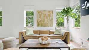 Een moderne woonkamer met een beige bank, een bijzettafeltje met decoratieve objecten en een groot abstract schilderij.