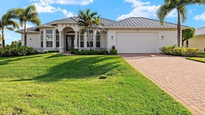 A modern two-story house with a garage, surrounded by well-maintained lawns and palm trees.