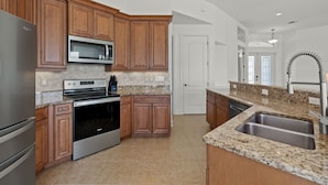 A modern kitchen with wooden cabinets, stainless steel appliances, granite countertops, and a large island with a sink.